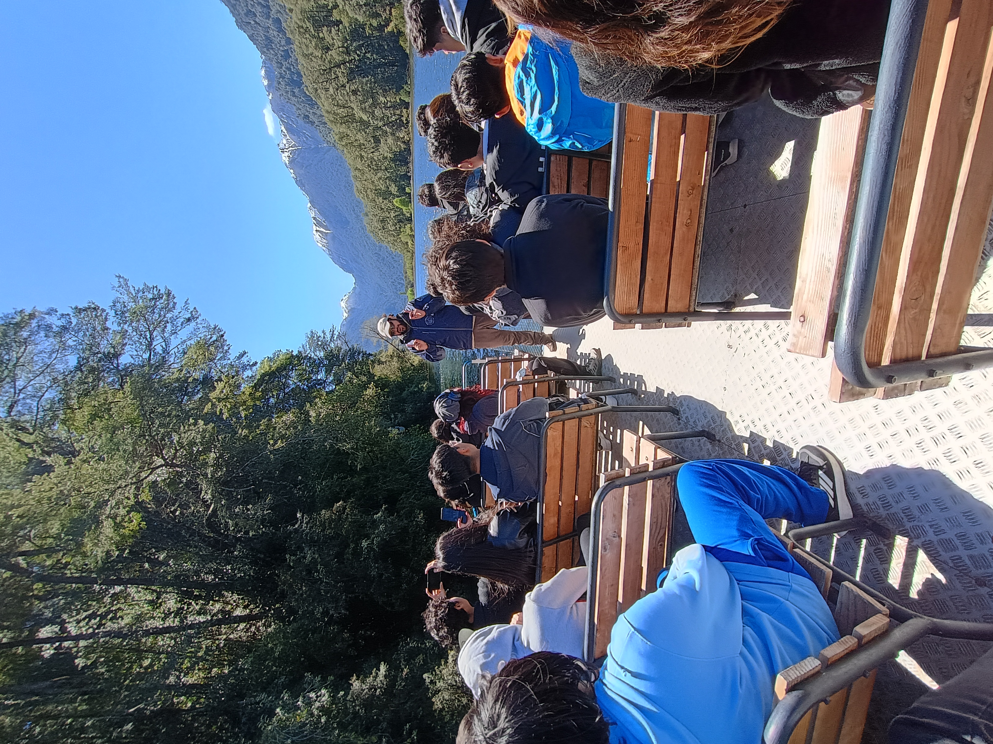 Estudiantes del liceo sentados junto al lago rodeados de montañas durante una salida pedagógica