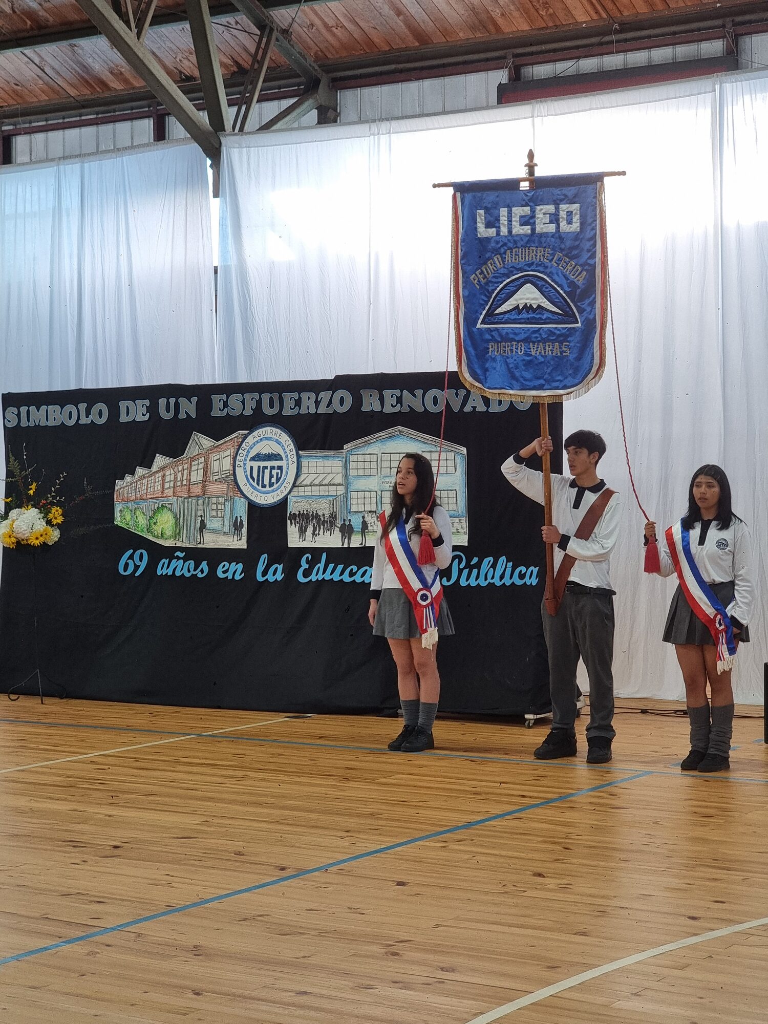 Escolta de banderas frente al banner de aniversario del liceo