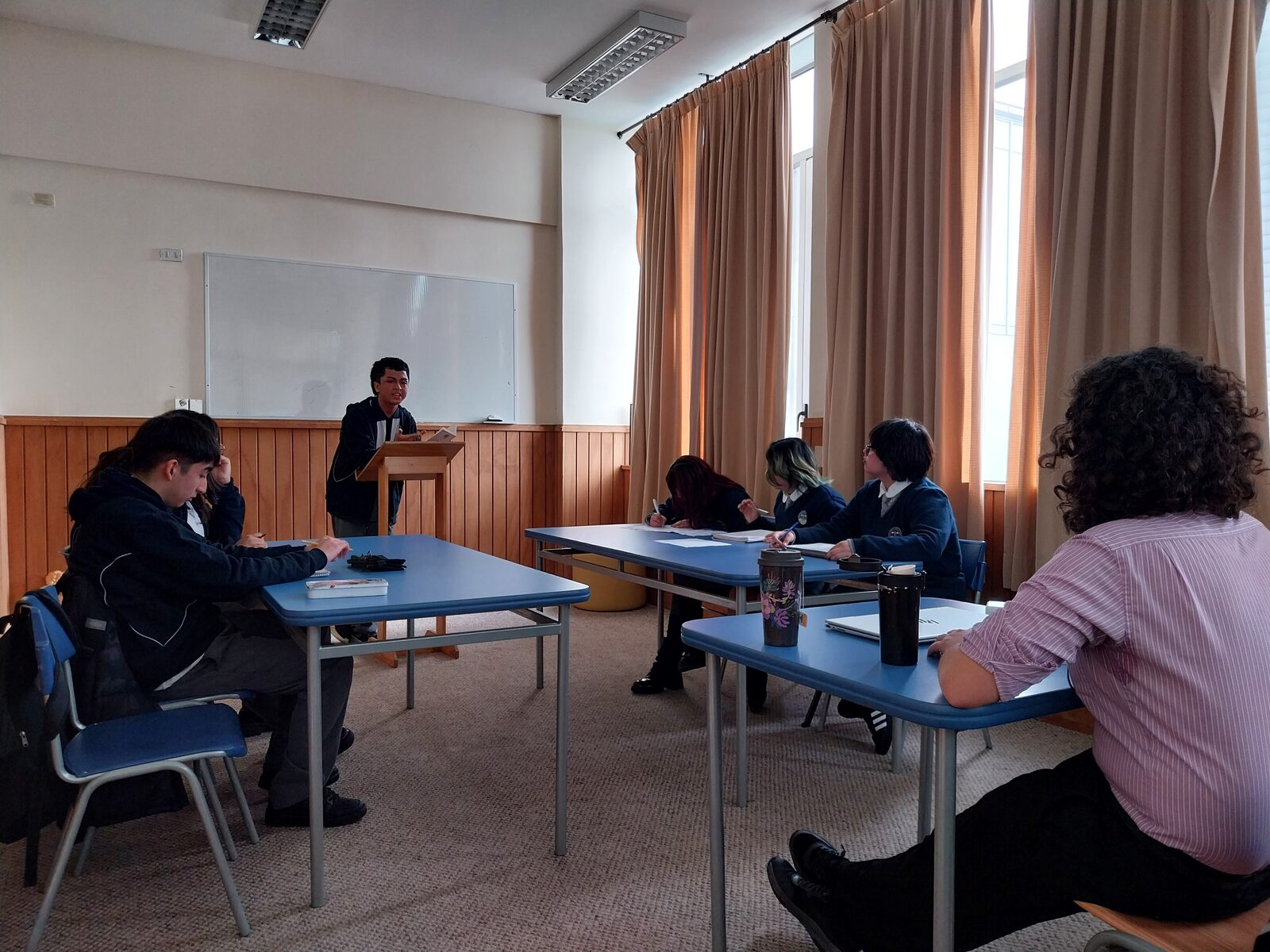 Estudiantes en una sala del liceo durante una ronda de debate, con un expositor tras el atril