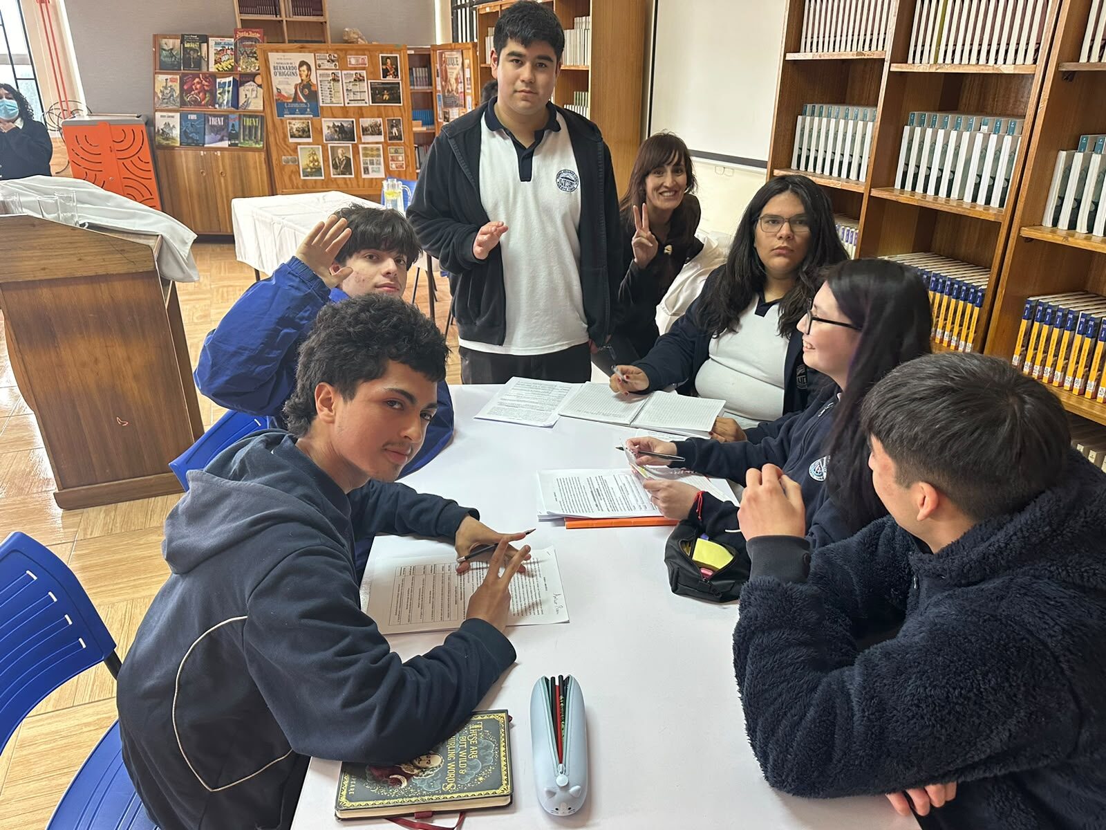 Estudiantes del taller de debate preparando sus argumentos en torno a una mesa, con libros al fondo