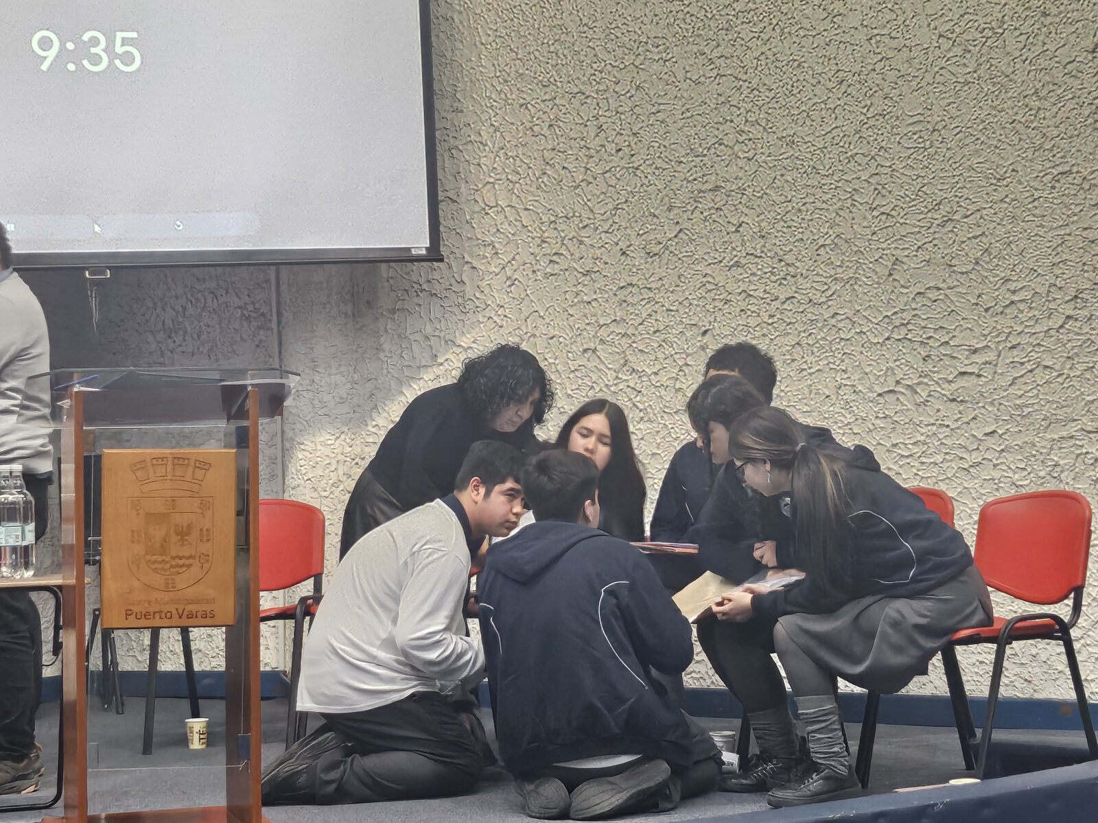 Estudiantes conversando en el escenario del auditorio mientras preparan su intervención